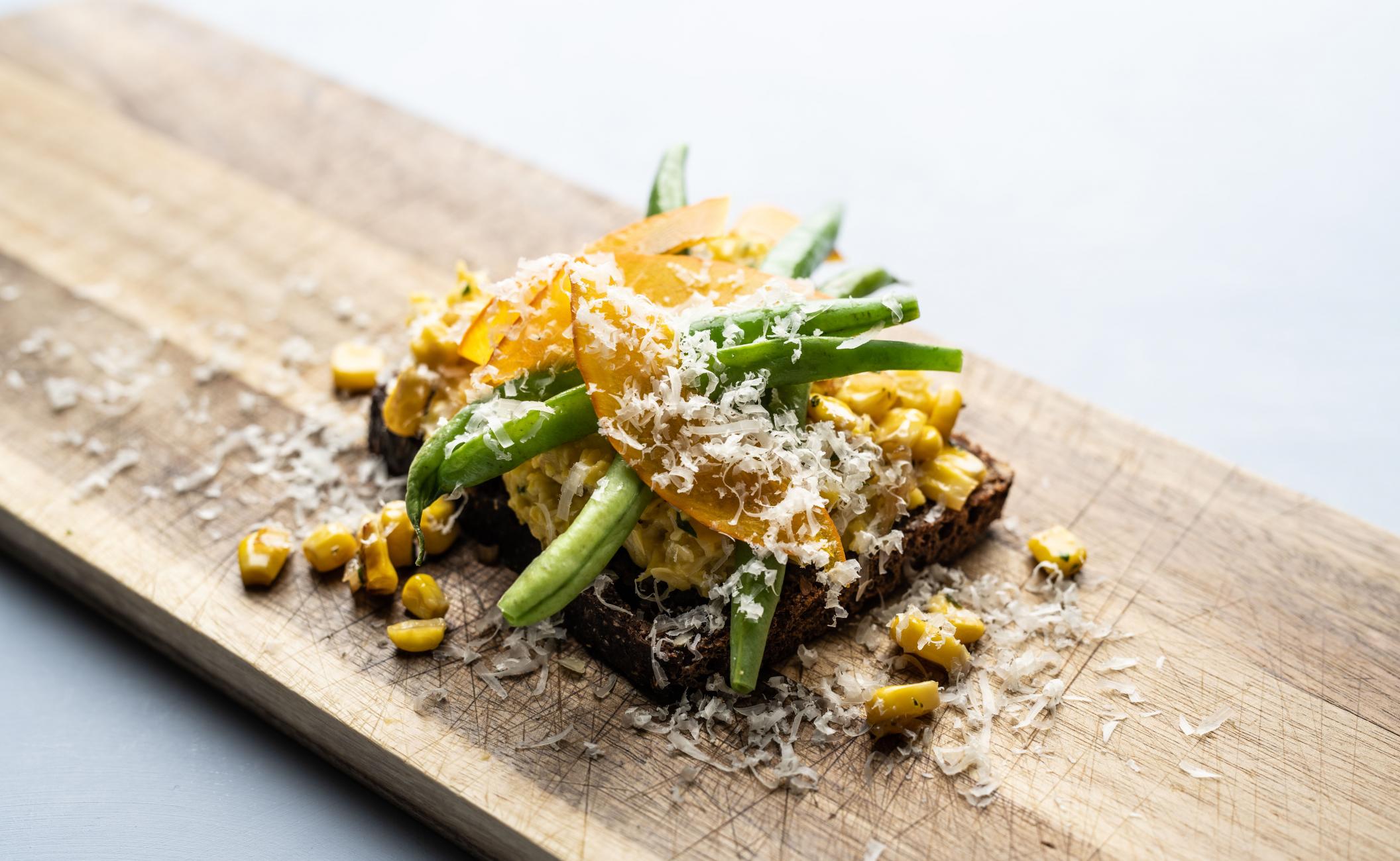 Grov majscreme på rugbrød, toppet med grønne bønner og parmesan